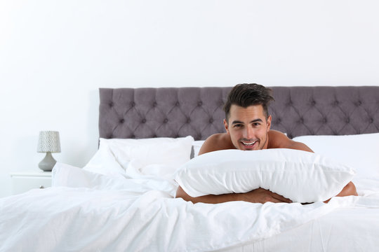 Sexy young man with soft pillow on bed at home