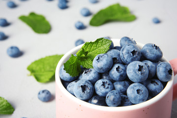 Cup with juicy blueberries and green leaves on color table