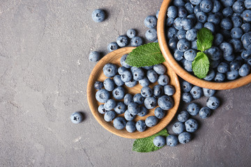 Flat lay composition with juicy blueberries and green leaves on color table. Space for text