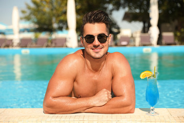 Young man with cocktail in pool on sunny day