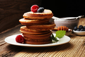 Pancakes with berries and maple syrup on rustic table