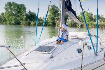Obraz premium Funny little baby captain on board of sailing yacht watching offshore sea on summer cruise. Travel adventure, yachting with child on family vacation. Kid clothing in sailor style, nautical fashion.