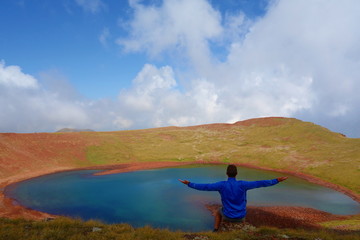 Fototapeta premium Young man sitting at the edge of Azhdahak volcano with a turquoise lake hidden inside in Geghama mountains, Armenia