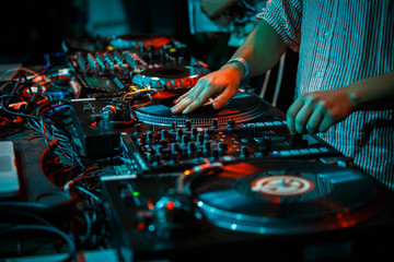 Hip hop DJ scratches vinyl record on turntable. Disc jockey scratching records with sound mixer and turntables in nightclub. Disk jokey mixing muisc set on stage in the club - obrazy, fototapety, plakaty