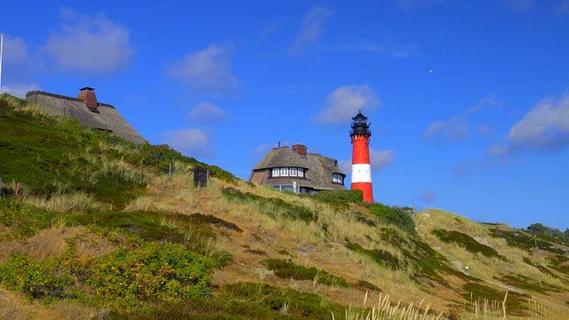 Leuchtturm H&ouml;rnum Sylt mit D&uuml;nen Landschaft  Reetdach H&auml;usern und  blauen Himmel
