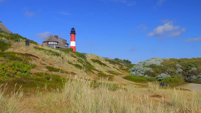 Leuchtturm H&ouml;rnum Sylt mit D&uuml;nen Landschaft  Reetdach H&auml;usern und  blauen Himmel
