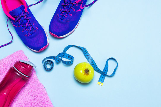 Fitness concept with Ultra violet pink female sneakers, water bottle, towel, apple on pastel blue background flat lay top view. Sports shoes, fitness, concept of healthy lifestile.
