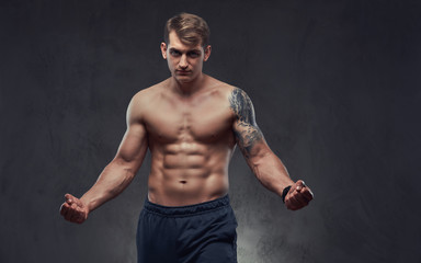 Young handsome shirtless sportsman with muscular torso and tattoo on his hand pose in a studio on a dark textured background.