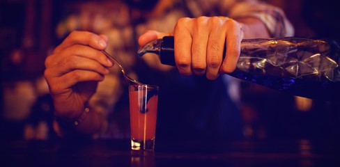 Waiter pouring cocktail drink into shot glasses at counter 