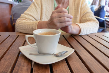An elderly woman sitting by the table with a cup of coffee in a restaurant.