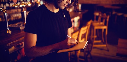 Young barman writing on diary