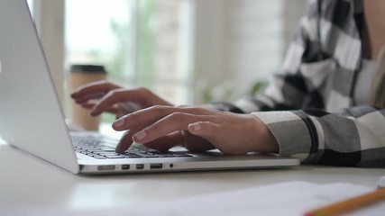 Successful business owner businesswoman typing on laptop, working at table in home office, young female professional is doing work, sitting in comfortable workplace with coffee cup in bright interior