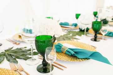 Interior of tent for wedding diner, ready for guests. Served round banquet table outdoor in marquee decorated hydrangea flowers, Golden dishes and green napkins. Catering concept
