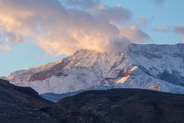 Sunset image of snow covered mountain partially covered by clouds