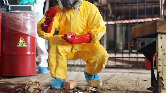 Caucasian man in red rubber gloves taking material for laboratory research. Slavic scientists working in abandoned building. Invisible danger. Indoors.