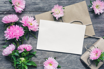 blank white greeting card with pink aster flowers, buds and gift box over rustic wooden background. flat lay. mock up