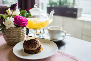 Chocolate truffle cake dessert with white chocolate. Pineapple tea with a transparent glass teapot. Citrus vitamin tea and a beautiful bouquet of flowers with roses, daisies and tulips on the table.