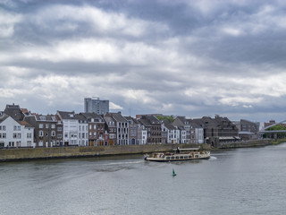Obraz premium View to the Meuse River with a ship and beautiful old buildings against a moody overcast sky in Maastricht, Netherlands