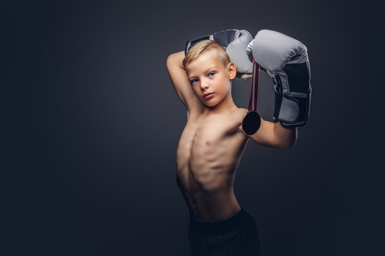 Young shirtless boy boxer in boxing gloves holds a golden medal posing in a studio.