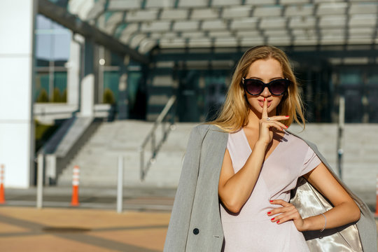 Delightful young woman wearing sunglasses and showing silence gesture. Space for text