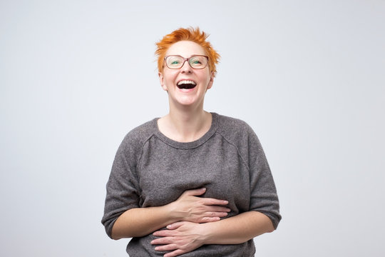 Close up portrait of a beautiful mid adult woman with red hair laughing standing on gray background. She is impressed and out of mind