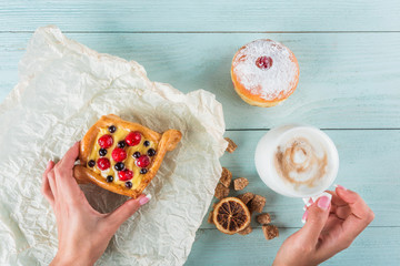 Hands holding a cup of coffee and a cake