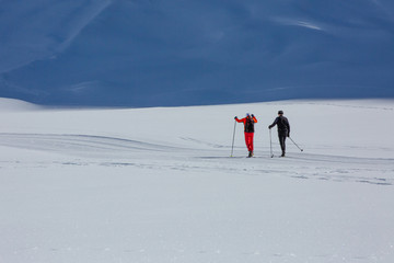 Two skiiers walk trough snow valley ion Alps