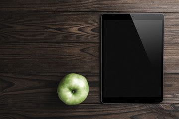 Tablet and green apple on brown wood background with copy space and text space, top view
