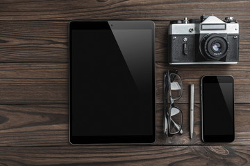 Old retro camera, tablet, silver pen, eyeglasses and smartphone on vintage wooden background. Top...