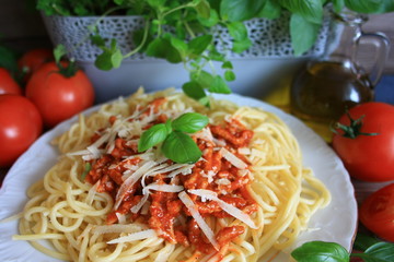 Makaron z sosem spagetti na białym talerzu na tle donicy z ziołami, oliwy i pomidorów