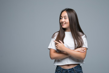 Young asian girl pointing on copyspace and looking at the camera over gray background
