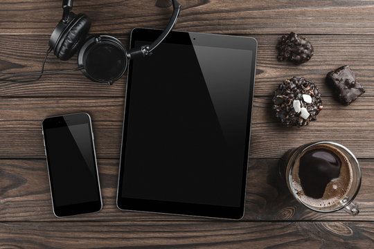 Top view of a tablet in high definition, headphones, smartphone, sweets and coffee on a wooden office table background