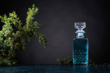 Blue gin in crystal decanter and juniper branch with berries. - obrazy, fototapety, plakaty