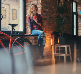 Pensive sensual blonde hipster woman with long curly hair dressed in a fleece shirt and jeans holds...
