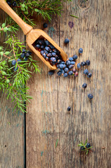 Juniper branch and wooden spoon with berries on a wooden background.