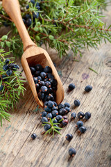 Juniper branch and wooden spoon with berries on a wooden table.