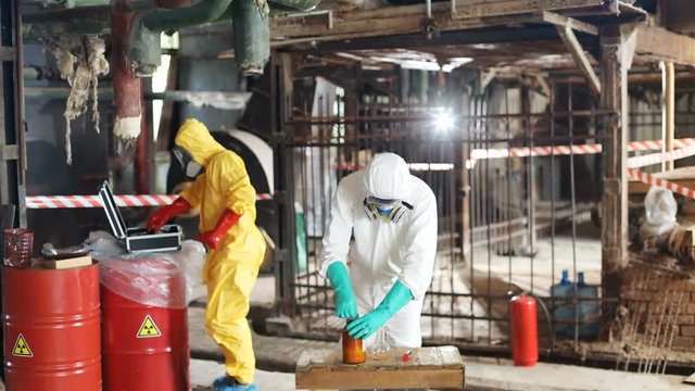 Two men in colored protective suits and gas masks spending time in abandoned nuclear power station. Ecologists using glassware at work. Environment.