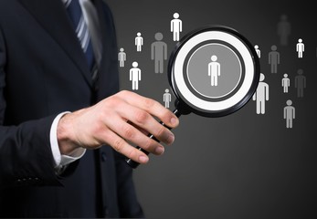 Human hand holding magnifying glass searching people icons on