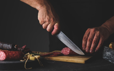 Men's hands cut sausage salami on a cutting board.