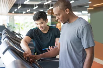 Fotobehang Persoonlijk Black man setting up exercise machine with personal trainer. Serious young guy training in gym. Workout concept.  © Mangostar