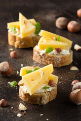 Canapes on bread with cheese, hazelnuts, Basil. Delicious appetizer with nuts for wine. Vegetarian gourmet food on dark background