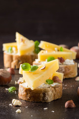 Canapes on bread with cheese, hazelnuts, Basil. Delicious appetizer with nuts for wine. Vegetarian gourmet food on dark background