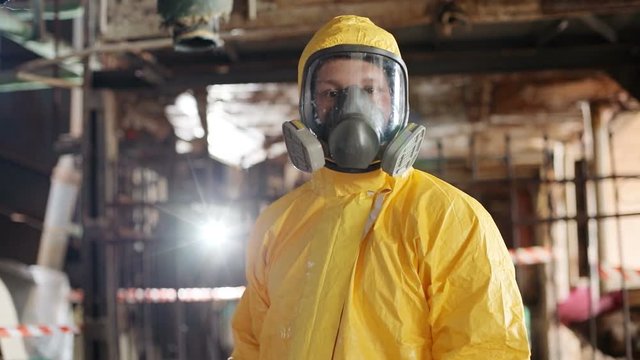 Portrait of young Caucasian guy wearing respirator mask and yellow hazmat suit. Slavic scientist with brown eyes looking at camera. Indoors. Radiation.