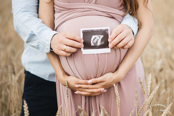 Close-up of unrecognizable pregnant woman with ultrasound picture in hand