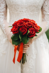 Beautiful wedding bouquet for the bride with red roses in the hands of the bride