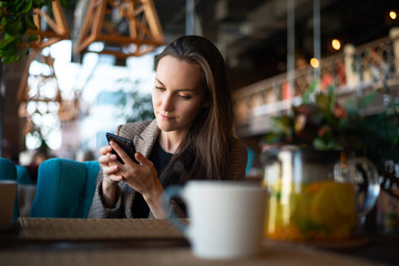 The girl uses a smartphone in his hands at the table in the restaurant