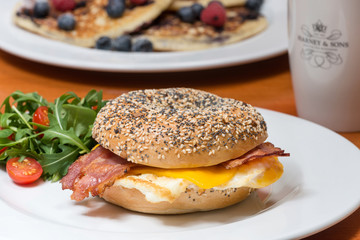 Tasty fresh bagel with bacon, egg and cheese. Pancake in behind.