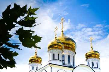Fototapeta na wymiar White orthodox church with gold domes (cupolas) against the blue sky