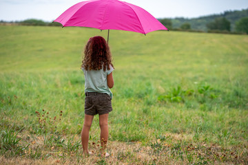 une petite fille se met à l'abris sous un parapluie rose