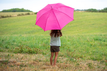 une enfant à l'abris sous un parapluie rose
